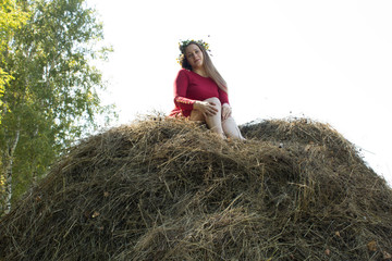 Naklejka na ściany i meble Blonde girl near a haystack. A wreath of flowers on the head. haymaking.