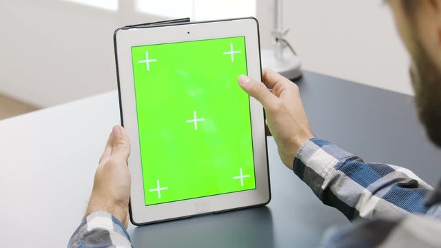 Man working on a digital tablet PC with green screen on it