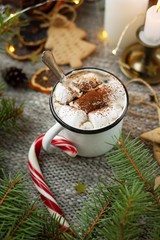 A beautiful coffee break in a festive, cozy atmosphere. A cup or mug of coffee or cocoa with marshmallows among fir branches, lights and Christmas decor.