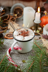 Obraz na płótnie Canvas Cozy coffee break in a festive Christmas atmosphere. A cup or mug of coffee or cocoa with marshmallows and Christmas cane among fir branches, candles, lights and other holiday decor.