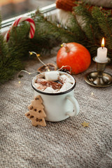 Obraz na płótnie Canvas Pumpkin latte, cappuccino or cocoa with marshmallows in a white mug on a light knitted background near the window. Beautiful coffee break in a festive, cozy Christmas atmosphere