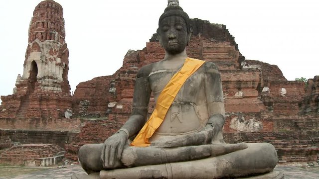 A wide, frontal shot of the Mara-posed sandstone image of Buddha at Wat Mahatthat, with the ancient red brick and stucco-finished Prang and Ubosot at the background.