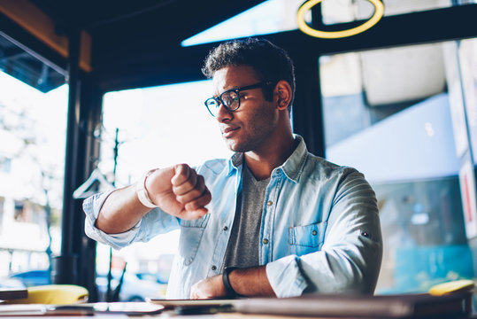 Mature handsome pondering male entrepreneur checking time on smartwatch while waiting for meeting with customer in coffee shop.Good looking man planning working schedule using digital device indoors
