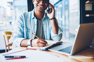 Half length portrait of smiling professional freelancer having mobile conversation with client on...