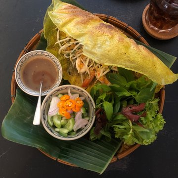 Banh Xeo. Sizzling crispy thin yellow pancake. Vietnamese food. Top-down composition. Dark table.