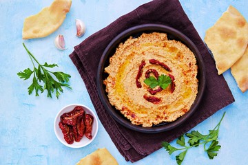 Hummus with sun-dried tomatoes in a brown clay bowl on a light blue concrete background. Served with tortillas, drizzled with olive oil when applying. Healthly food. Recipes chickpeas. Vegan food.