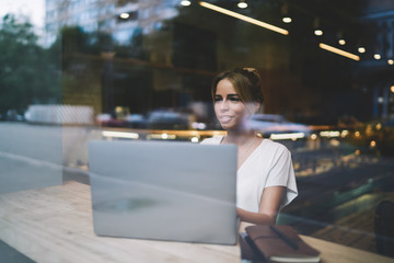 Positive female copywriter spending time at coworking space for working remotely on new project for...