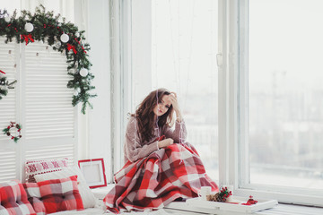 Beautiful young woman sitting in plaid by the window