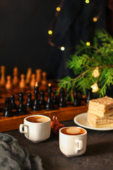 coffee, piece of cake (festive atmosphere, chess, Christmas lights, new year) menu concept. food background. top view. copy space