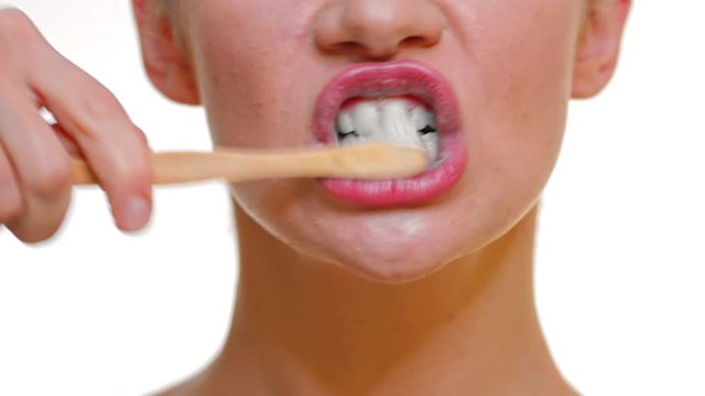 Closeup on the lips of a woman cleaning her teeth with a bamboo toothbrush and black carbon toothpaste.