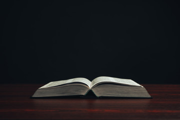 Open bible on a  red wooden table. Beautiful black background.