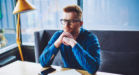 Thoughtful hipster guy in optical eyewear for vision correction pondering on ideo for university...