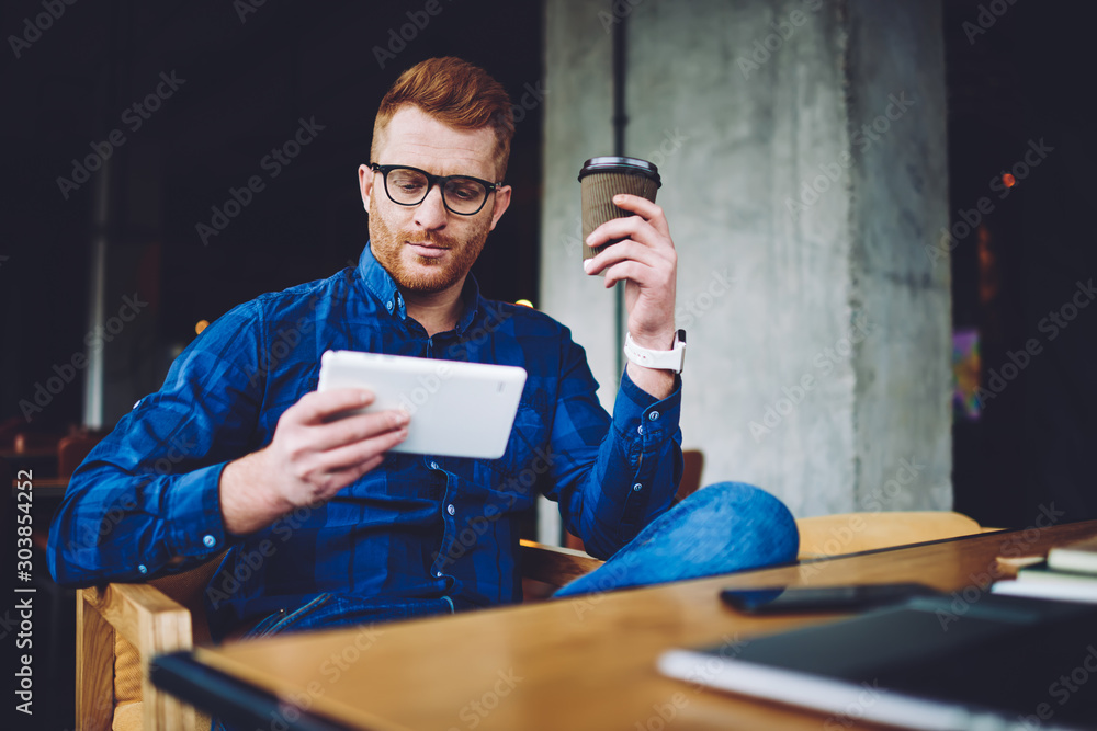 Poster caucasian male blogger reading received message from follower on web page during coffee time in cafe