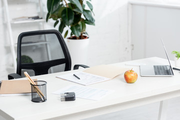 apple, stationery, documents and laptop on wooden table in clinic