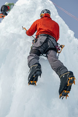 Fototapeta na wymiar Alpinist man with ice tools axe climbing a large wall of ice. Ou