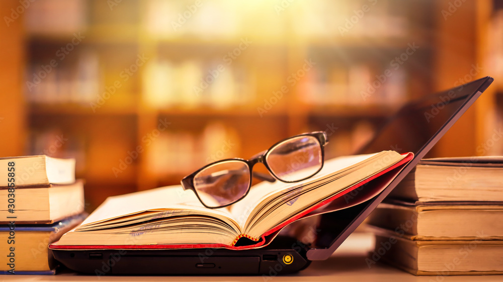 Poster stack of books with glasses placed on the open book in library.