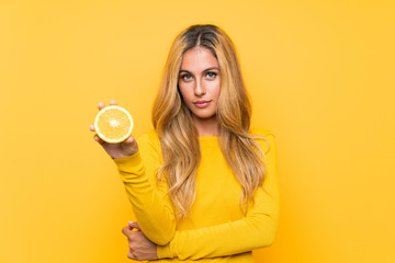 Young blonde woman holding an orange over yellow background