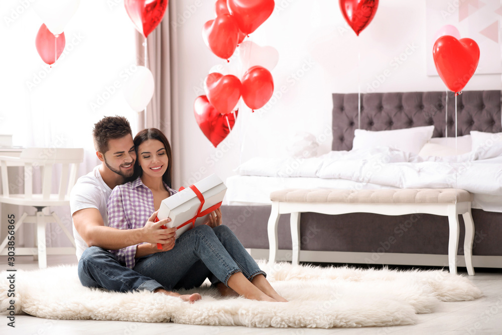 Wall mural Happy young couple in bedroom decorated with heart shaped balloons. Valentine's day celebration