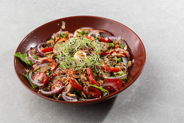 Veal salad with cherry tomatoes, mushrooms on a black plate on dark background. Plate on white background, copy space. Restaurant food, close up. Meat salad. Horizontal photo.