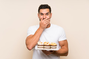 Handsome man holding muffin cake over isolated background with surprise facial expression