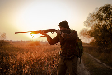 Young irish looking man with a reed, backpack and ammunition belt,  hunting at the countryside near the track in the picturesque sunset rays