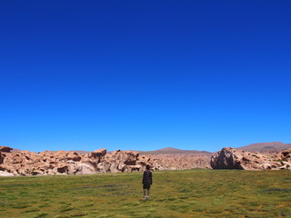 Fototapeta na wymiar A woman walking on green grass under a blue sky, Laguna Misteriosa, Journey from San Pedro de Atacama in Chile to Uyuni in Bolivia