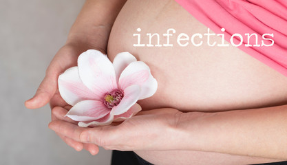 Obraz na płótnie Canvas Word INFECTIONS. Young pregnant woman keeps artificial orchid flower close to her belly.