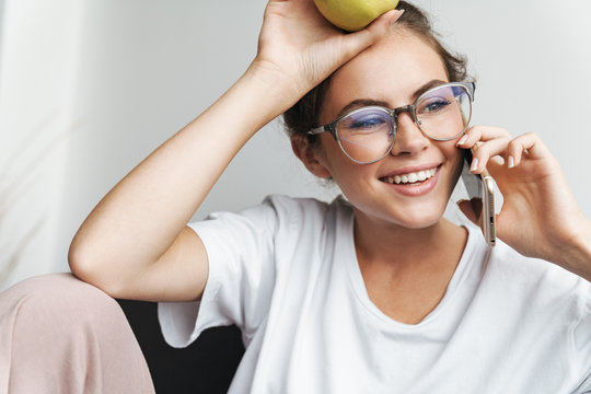 Image of smiling nice woman talking on cellphone and holding apple