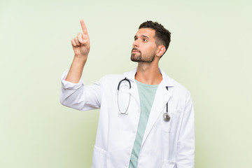 Young doctor man over isolated green wall touching on transparent screen