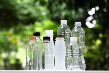 Many different shape drinking water bottles arrange into line with blur green garden background