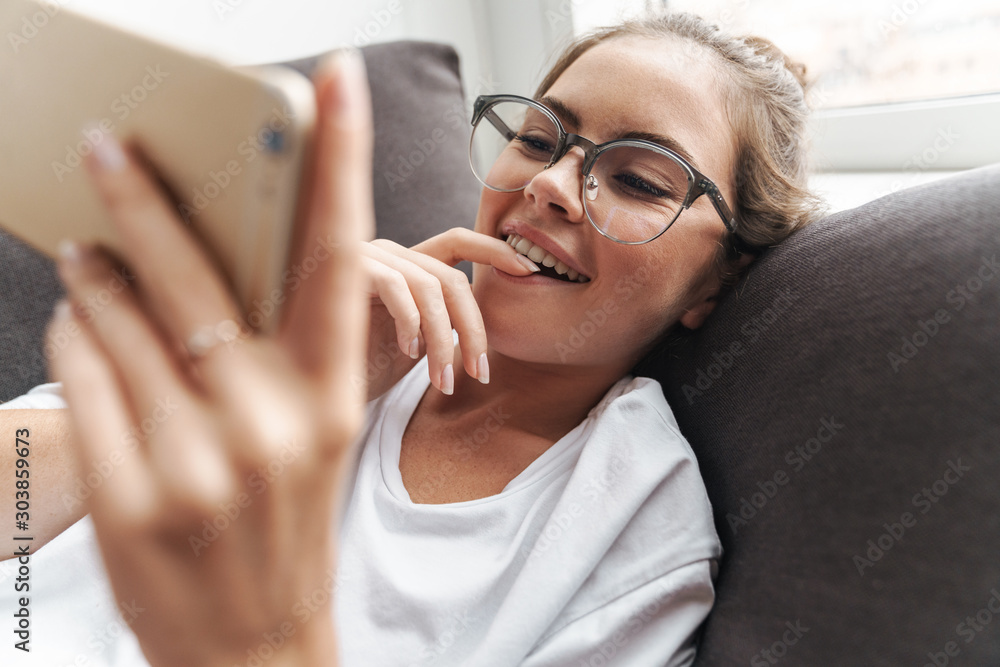 Poster image of concentrated woman smiling and using cellphone while lying