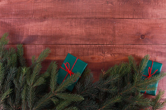 Fir Tree Branches And Green Gift Box With Red String And Bow On Brown Wooden Table. Christmas Background Concept. New Year, Winter Holiday, Copy Space, Top View, Border