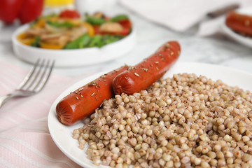 Tasty buckwheat porridge with sausages on table, closeup