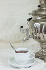 Metal samovar, white cup of tea and saucer on a light background. Carnival celebration concept. Traditional Russian tea party.