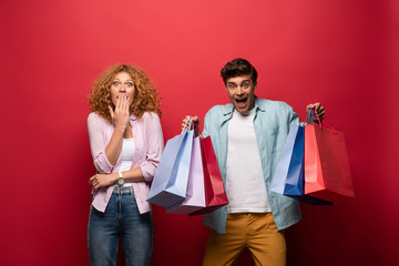beautiful surprised couple holding shopping bags, isolated on red