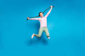 Fototapeta na wymiar Full length photo of positive cheerful millennial girl jump hold her braids have fun wear casual style outfit white sneakers isolated over blue color background