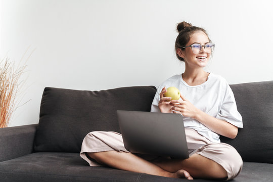 Image of smiling attractive woman holding apple and using laptop