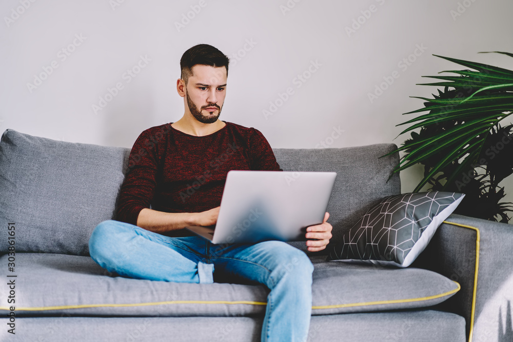 Poster pensive bearded young man freelancer watching tutorial online on internet websites using modern netb