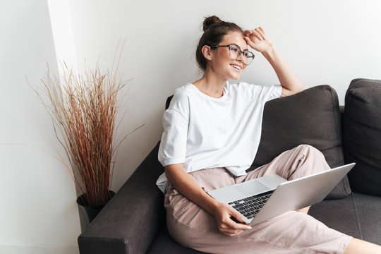 Image of happy beautiful woman using laptop while sitting on sofa