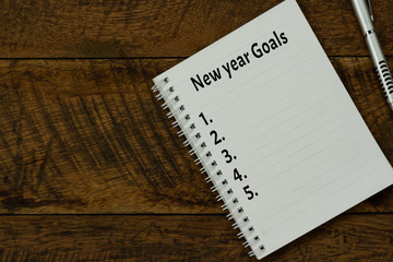 Table top view aerial image of 2020 new year business  goals & plans concept.Flat lay of essential object on brown wood.Text on notepad with black coffee and pen for accessories office desk backdrop