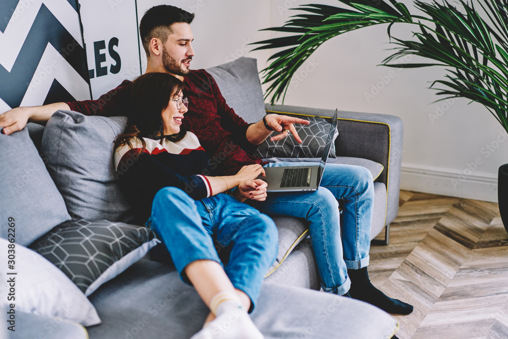 Poster young marriage discussing choose of movie relaxing together in modern apartment using laptop.girlfri