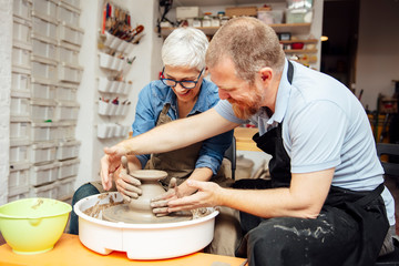 Senior woman spinning clay on a wheel with teacher at pottery class