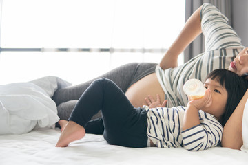 Happy asian family. Mother and daughter are playing tablet relax and fun. Mom and girl watch gadget sitting on the bed in the bedroom.