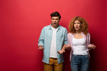 beautiful confused couple gesturing in casual clothes isolated on red