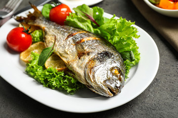 Delicious roasted fish with lemon and vegetables on dark grey background, closeup