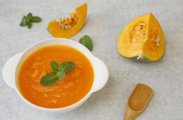 Pumpkin soup in a bowl on a white background with spoon, basil and slice of pumpkin. Menu, background, card. Healthy food concept. Top view. Food background.
