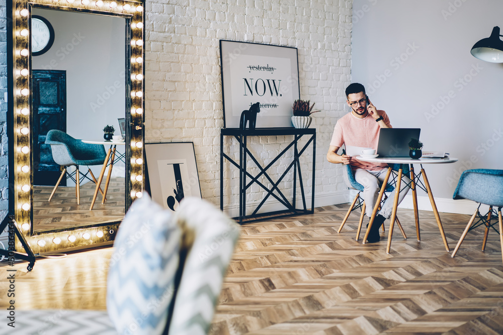 Aufkleber young man talking on smartphone while working remotely at modern netbook with wireless internet in m