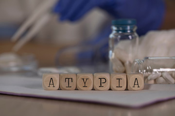 Word ATYPIA composed of wooden dices. Pills, documents and a pen in the background.