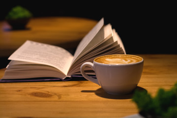 Ceramic cup of cappuccino in coffee shop with pattern on a wooden table with an open book. Latte art. Morning drink. Caffeine.