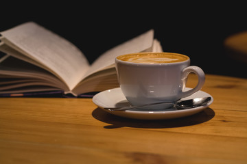 Ceramic cup of cappuccino in coffee shop with pattern on a wooden table with an open book. Latte art. Morning drink. Caffeine.